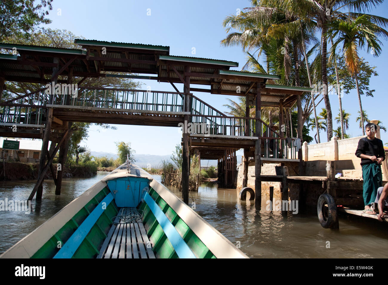 Ein Boot nähert sich eine hölzerne Brücke über einen Fluss in der Nähe von Indein, Inle Lake Area, Shan, Myanmar Stockfoto