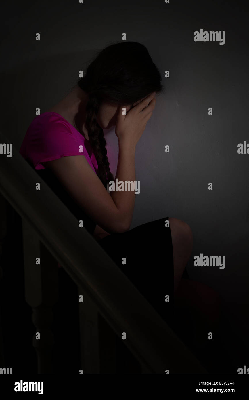 Launisch Schuss von eine junge Frau sitzt allein in der Dunkelheit, mit der Hand über ihr Gesicht. Depression und Stimmungen. Stockfoto