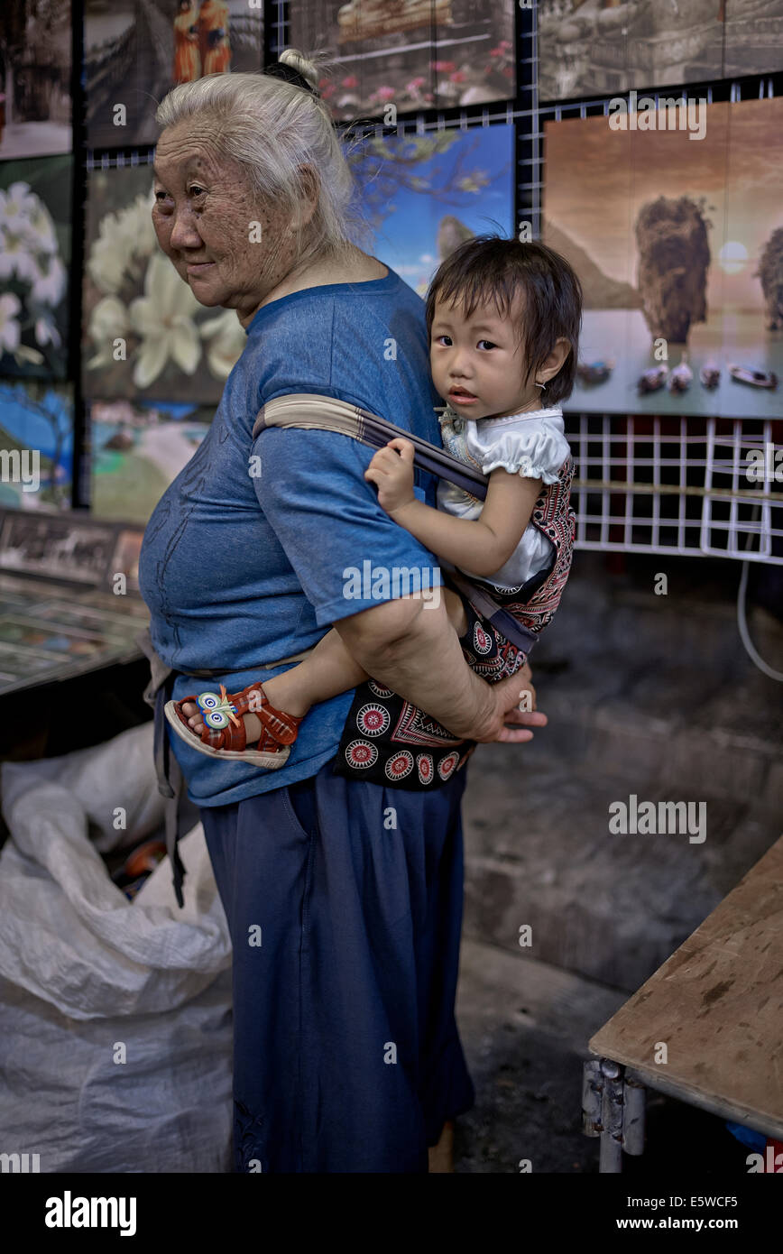 Großmutter, die Enkelin eines Kindes in einem Rückenschlingengurt mitführt. Thailand S. E. Asien, asiatische Oma mit Kind Stockfoto
