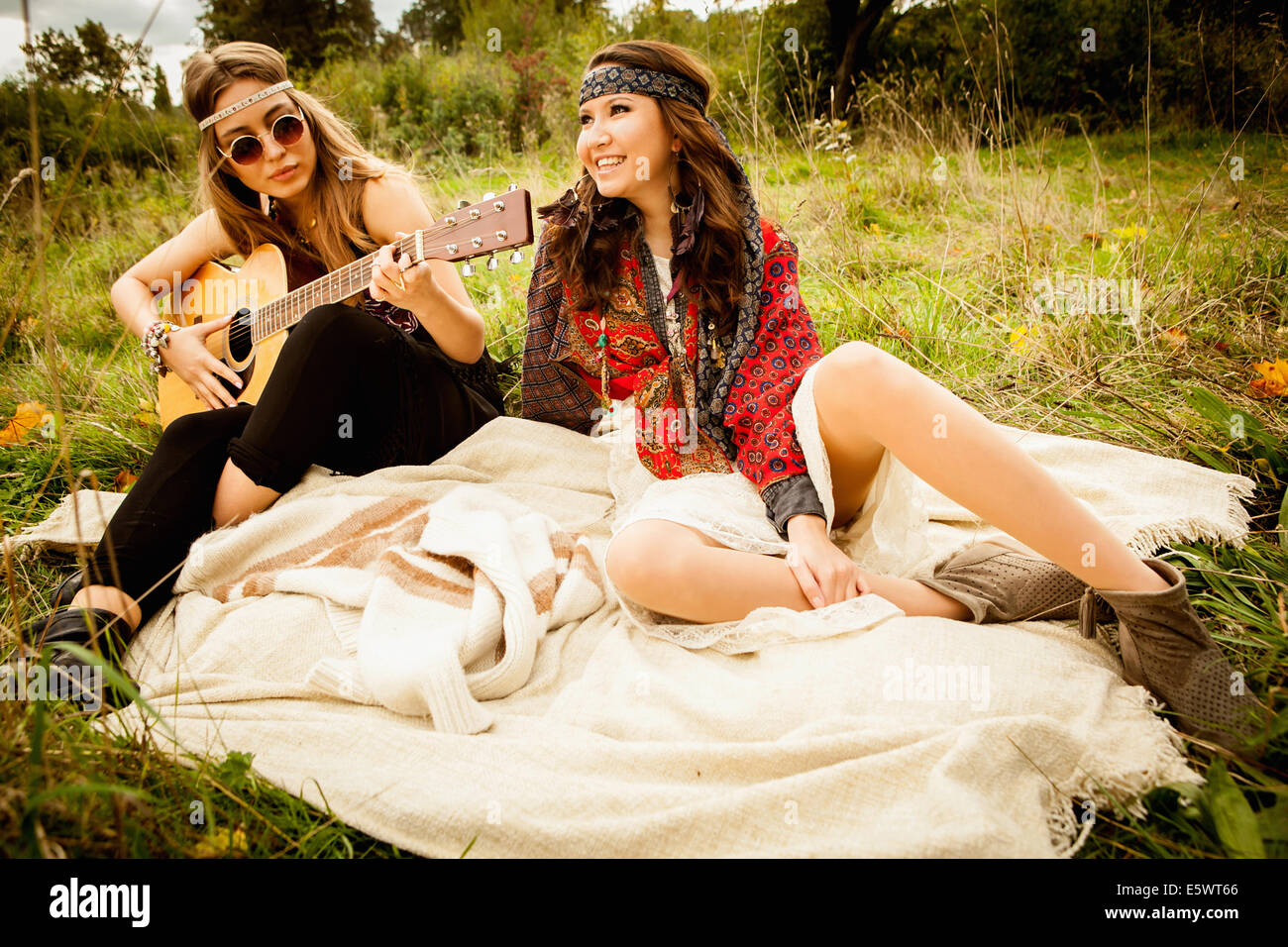 Hippie-Mädchen auf Decke im Feld, Gitarre spielen Stockfoto