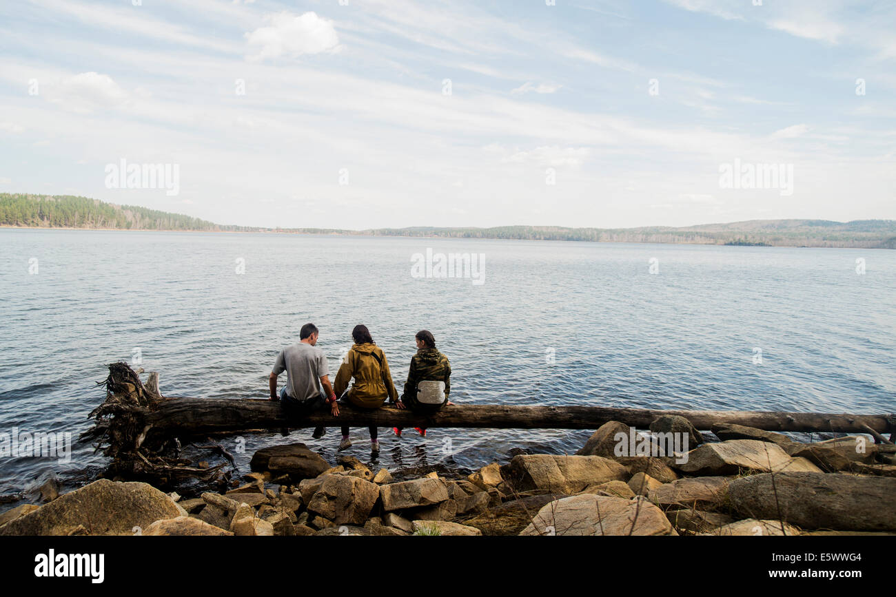 Drei Wanderungen Freunde sitzen in einer Reihe auf umgestürzten Baum am See Stockfoto