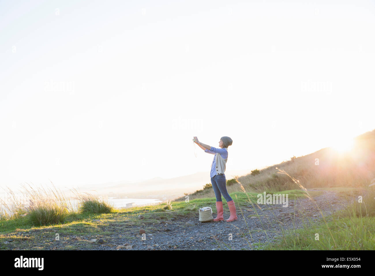 Junge Frau nehmen Foto auf Hügel bei Sonnenuntergang Stockfoto