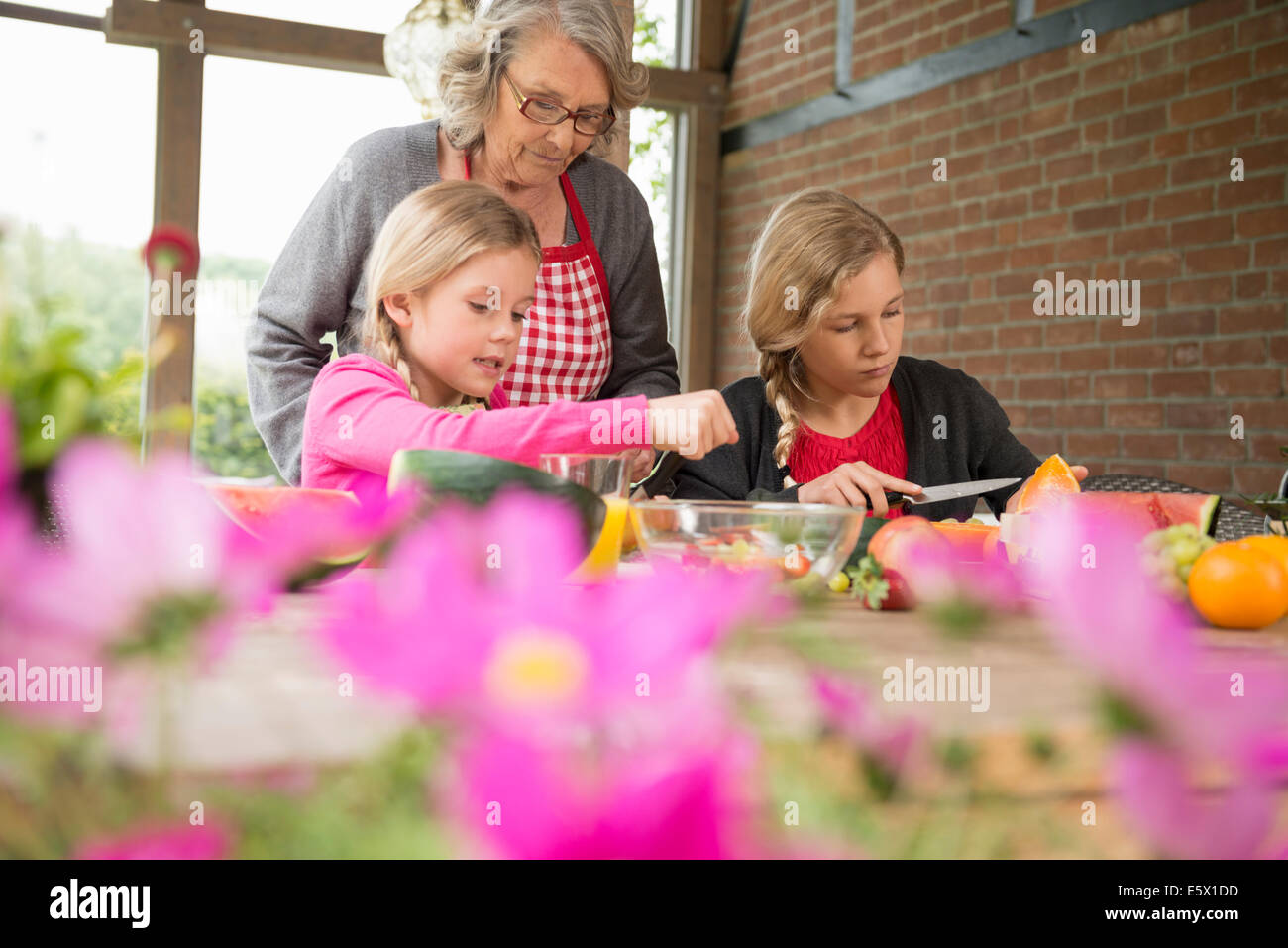 Zwei Schwestern und Großmutter Küche Tisch lernt, Scheibe frisches Obst Stockfoto