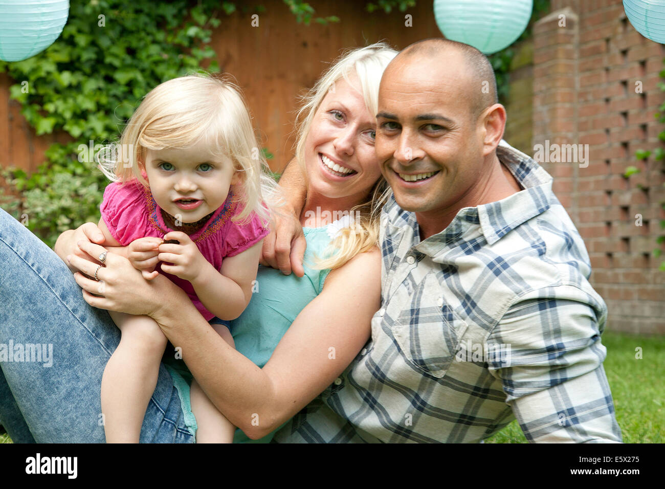 Porträt von glücklichen Paar mit Kleinkind Tochter im Garten sitzen Stockfoto