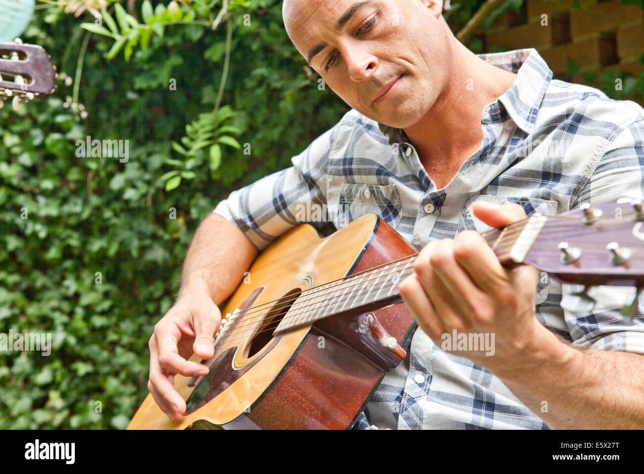 Mitte erwachsener Mann spielt akustische Gitarre im Garten Stockfoto