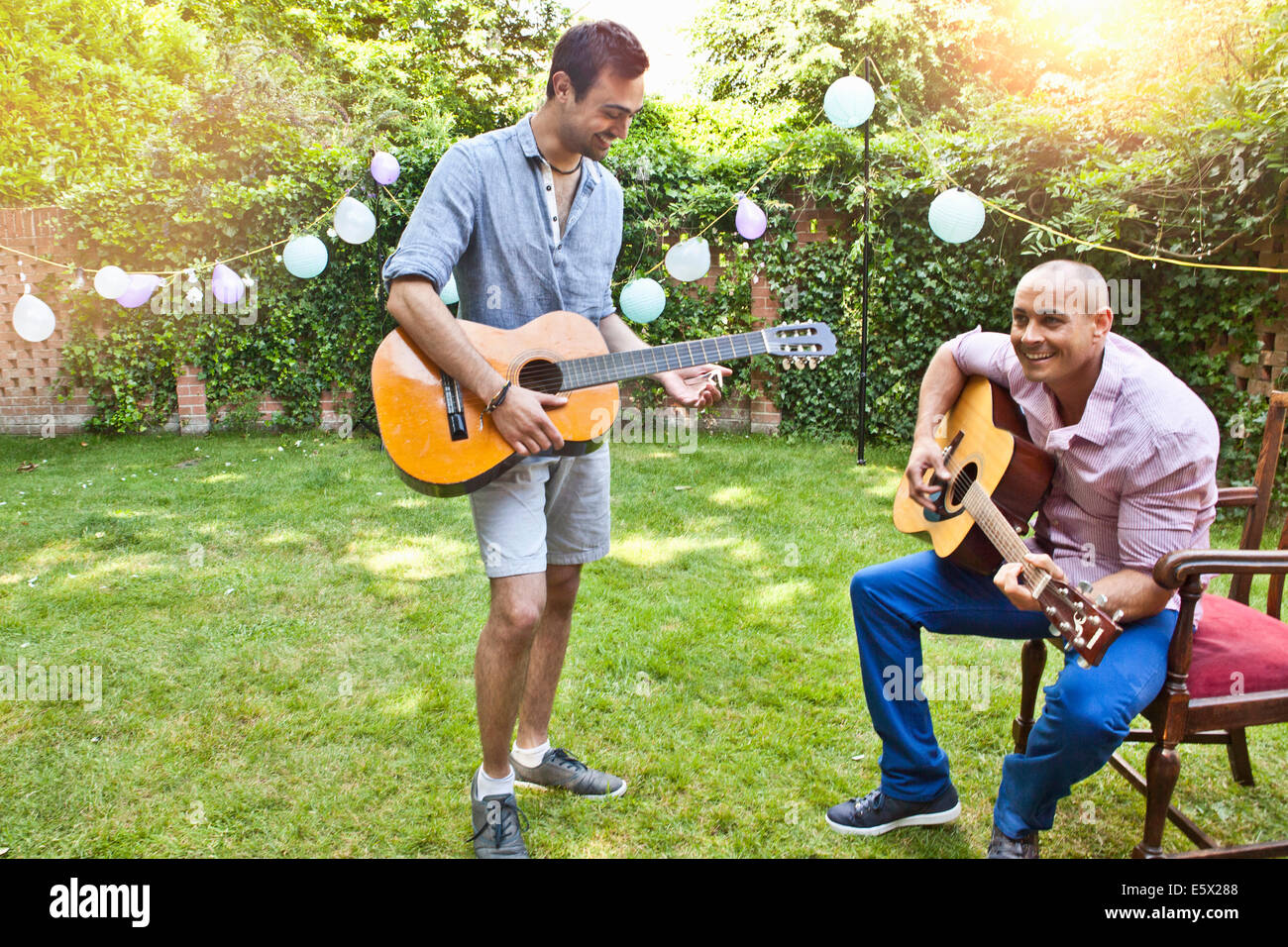 Zwei männliche Freunde spielt akustische Gitarre im Garten Stockfoto