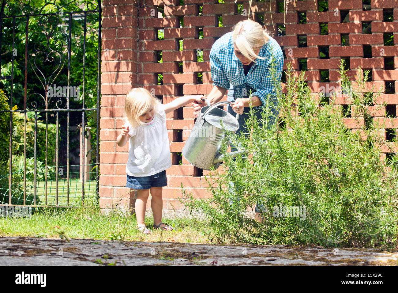 Weiblichen Kleinkind helfen Mutter mit Gießkanne im Garten Stockfoto