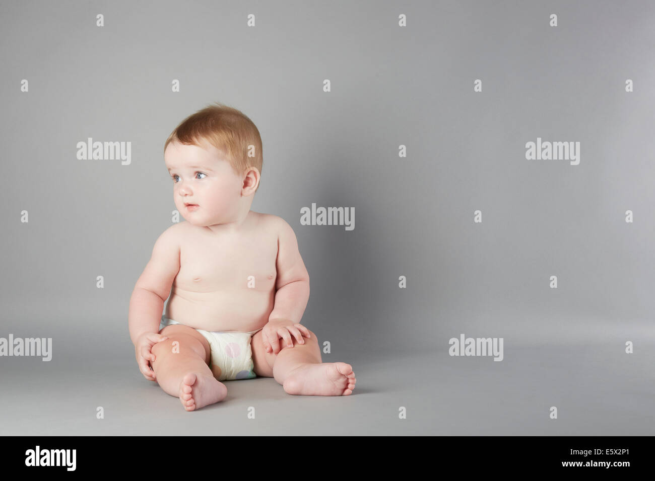Studioportrait von neugierigen Babymädchen sitzend Stockfoto