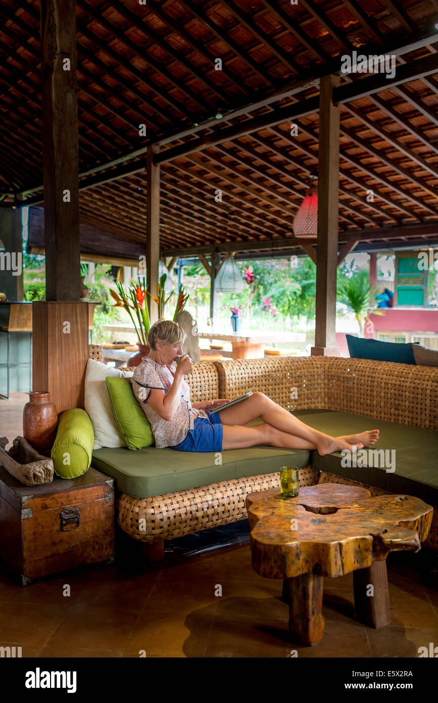 Frau, entspannend, mit Kaffee und digital-Tablette in Urlaub Wohnung Wohnzimmer, Ubud, Bali, Indonesien Stockfoto