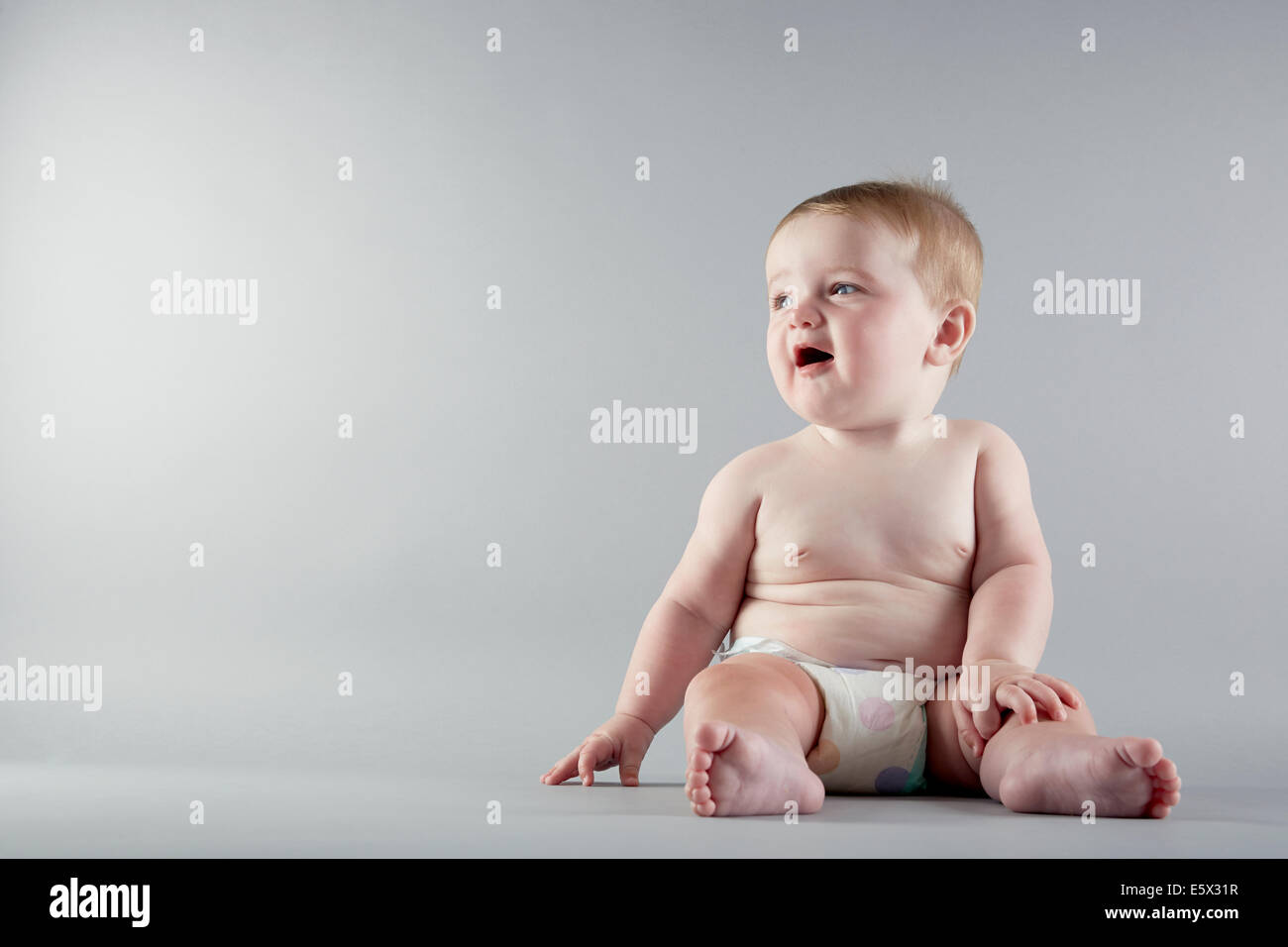 Studioportrait von Babymädchen sitzen und wegsehen Stockfoto