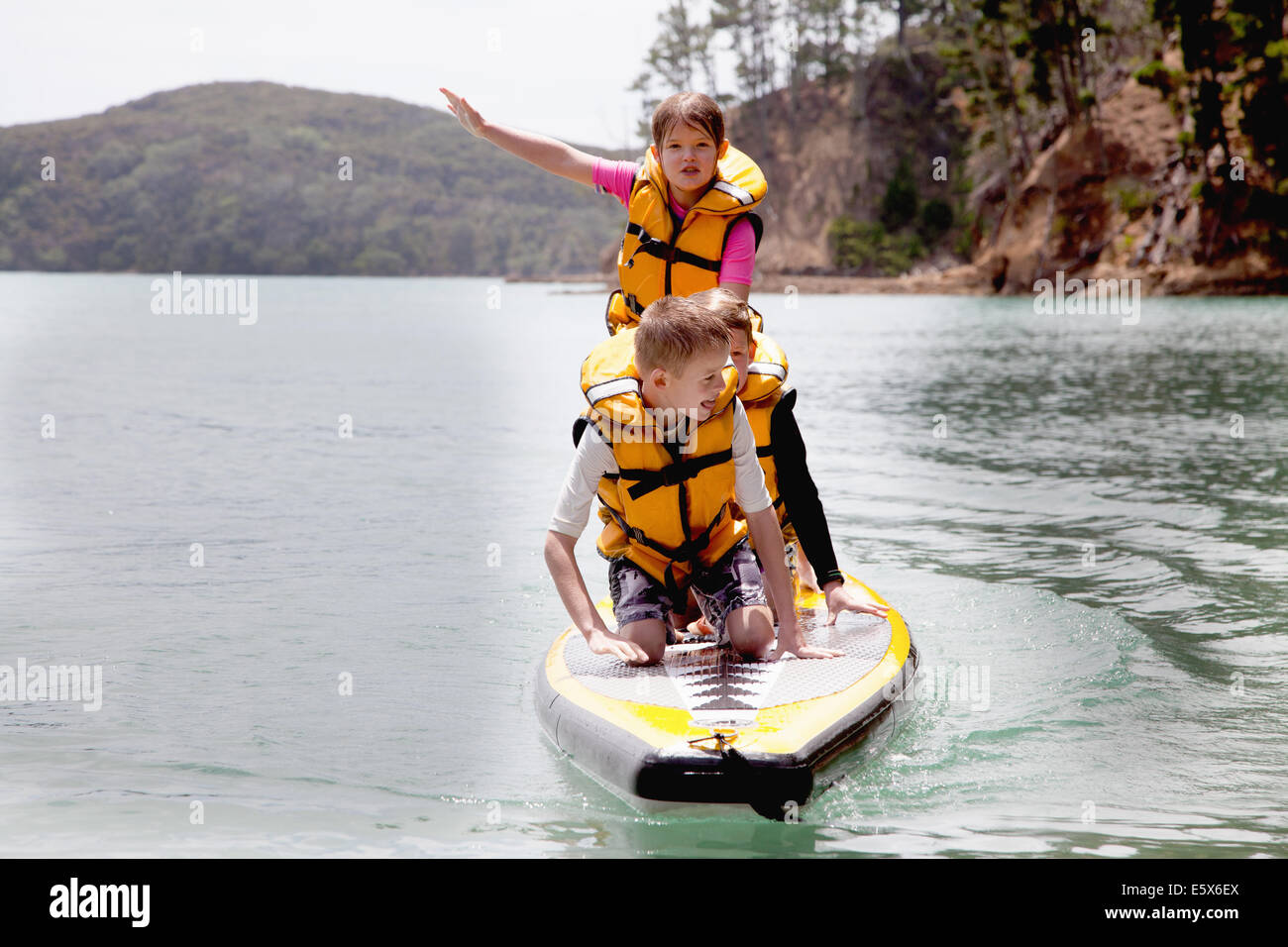 Brüder und Schwester, stehend und kniend auf Paddleboard auf hoher See Stockfoto