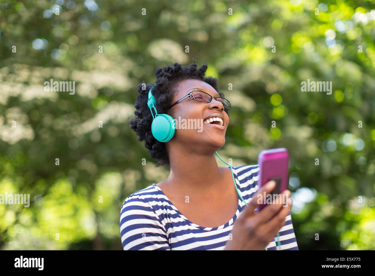 Junge Frau im Park hören und Singen Musik über Kopfhörer Stockfoto