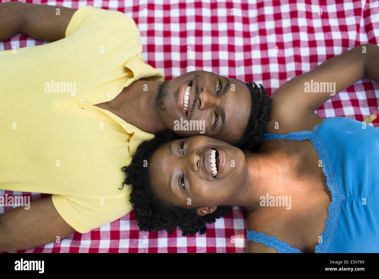 Obenliegende Porträt des jungen Paares auf der Picknickdecke auf gegenüberliegenden Seiten liegend Stockfoto