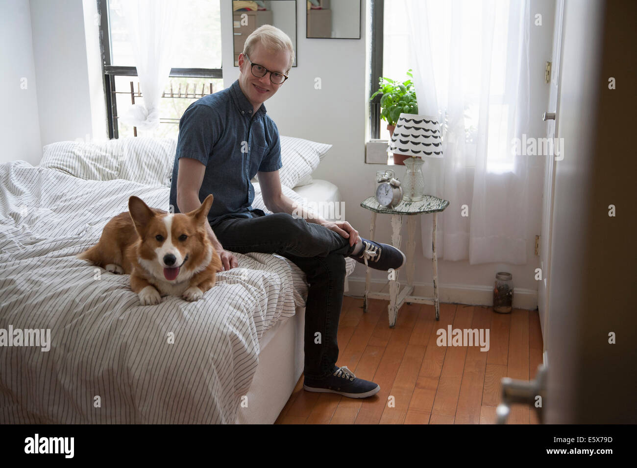 Niedliche Corgi Hund auf Bett liegend beobachtet von junger Mann Stockfoto