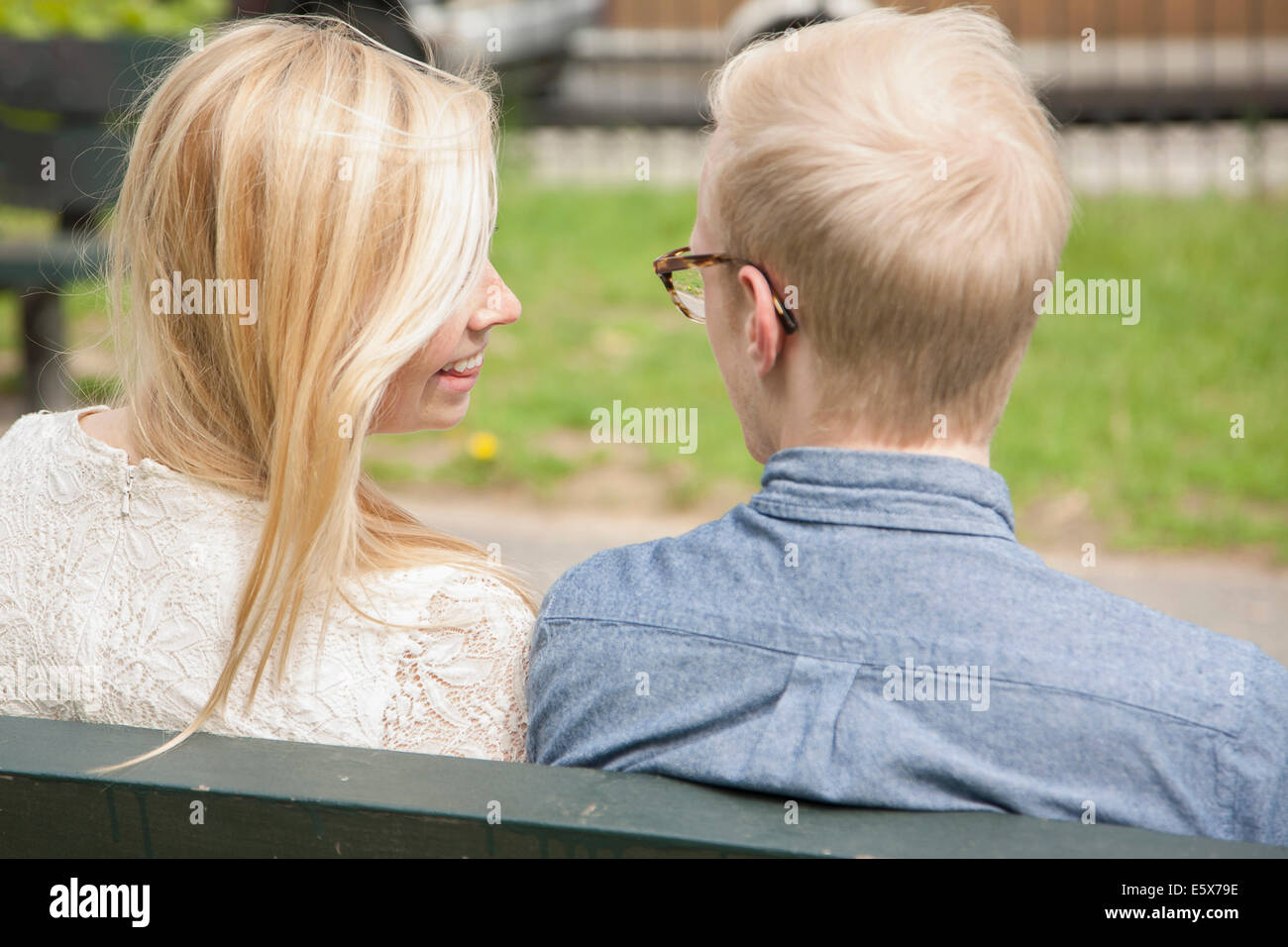 Über die Schulter-Blick des jungen Paares auf Parkbank Stockfoto