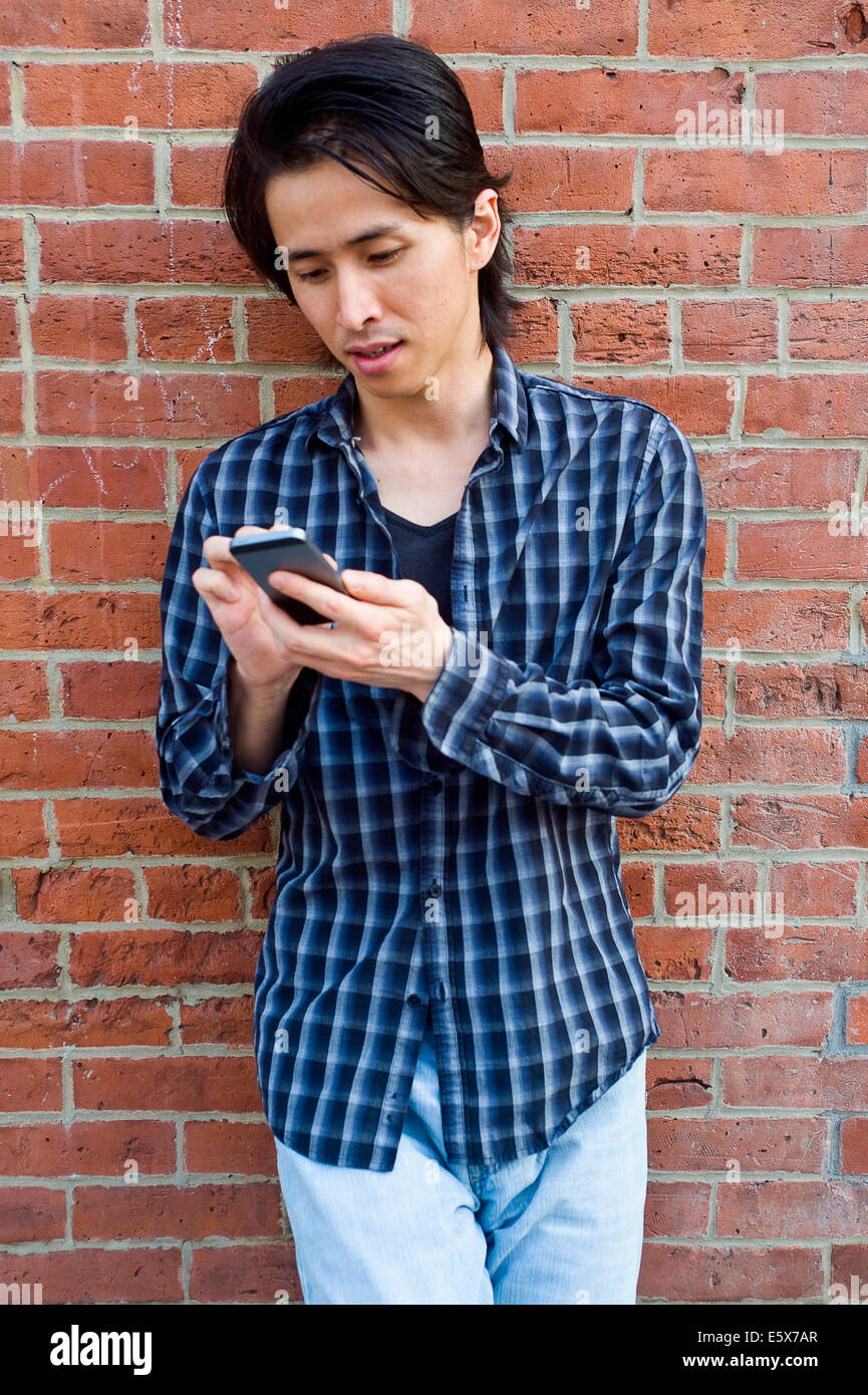 Mitte erwachsener Mann gelehnt Wand SMS auf smartphone Stockfoto