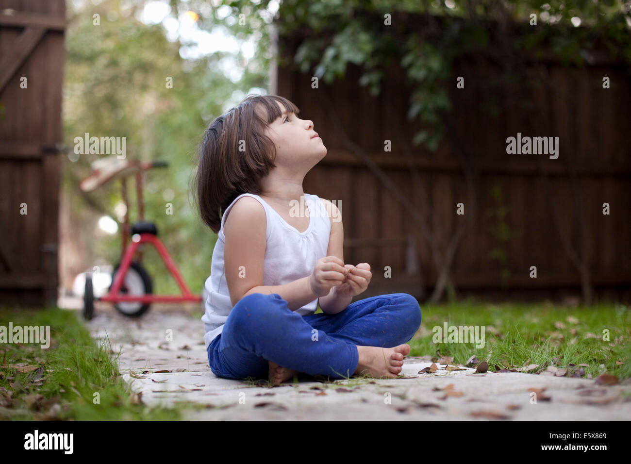 Vier Jahre altes Mädchen sitzen auf Gartenweg blickt nach oben Stockfoto