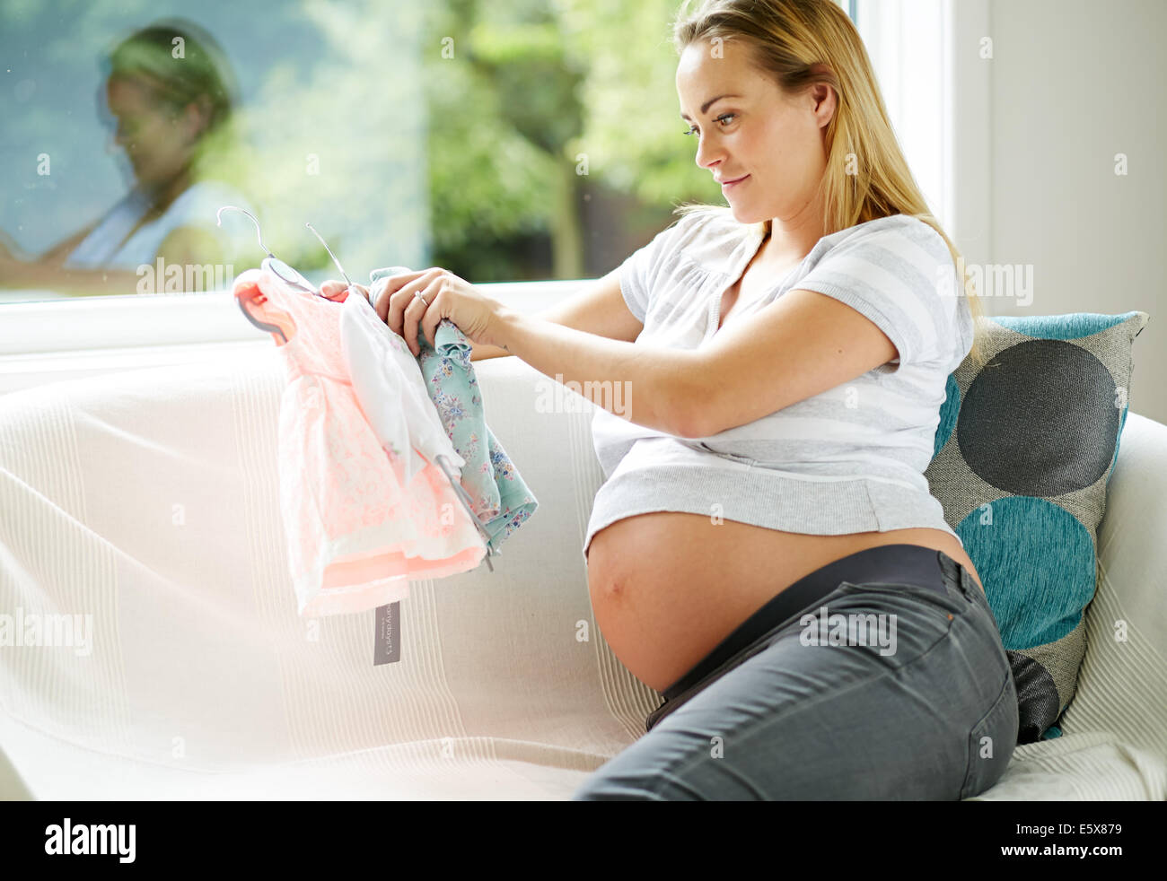 Schwangere Frau betrachten Baby-Kleidung Stockfoto