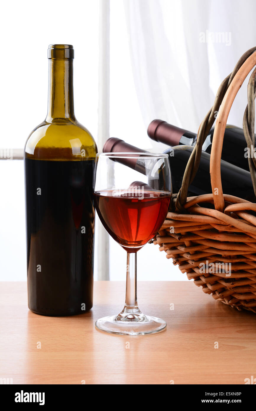 Wein Stillleben mit einem Korb voller Flaschen und einem Glas Rotwein vor einem Fenster mit Vorhängen. Hochformat. Stockfoto