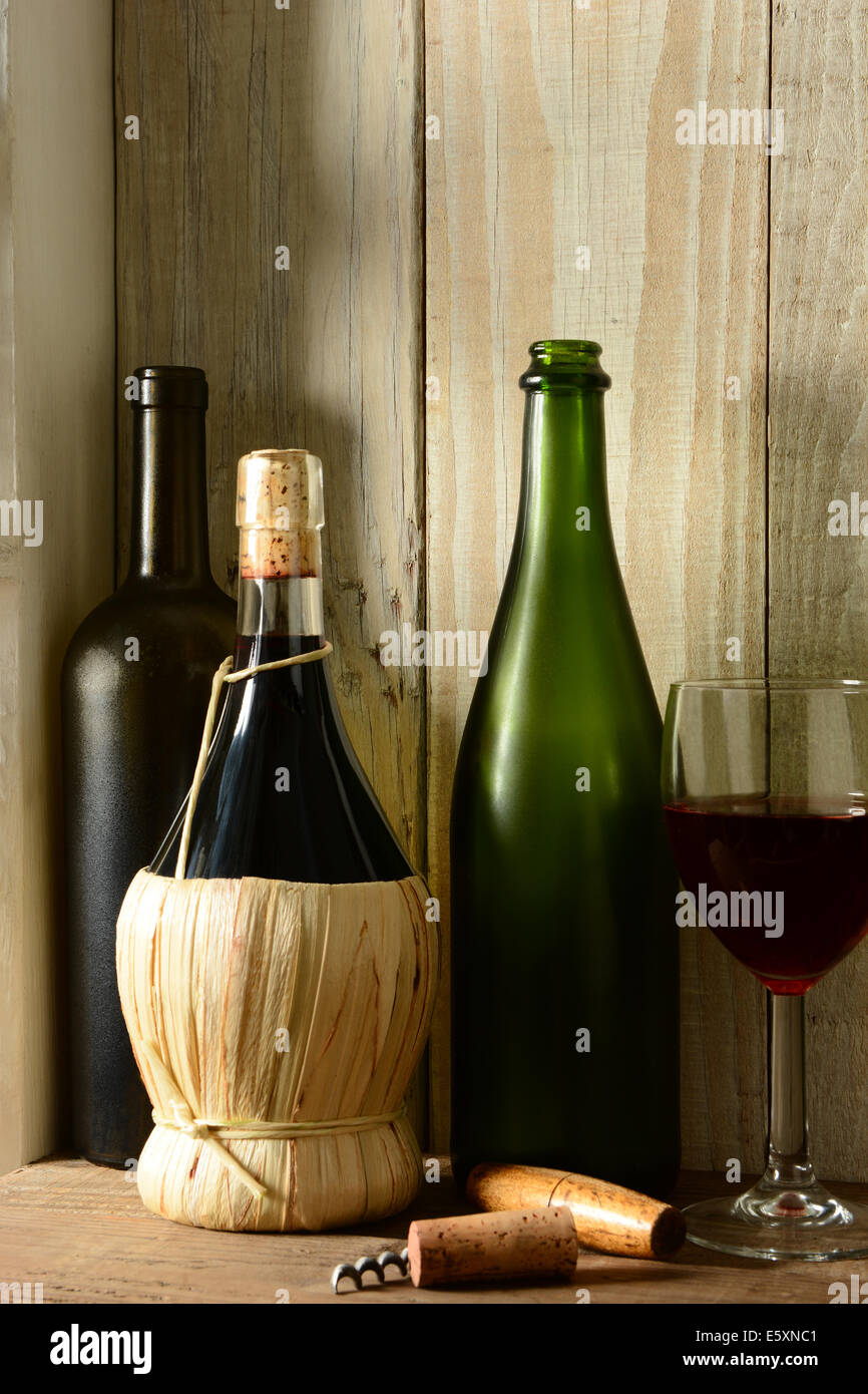 Ein Wein Stillleben mit warmem Licht aus einem Fenster auf der Seite. Drei Flaschen, ein Glas Wein und Kork Schrauben in einem rustikalen Rahmen, Ver Stockfoto
