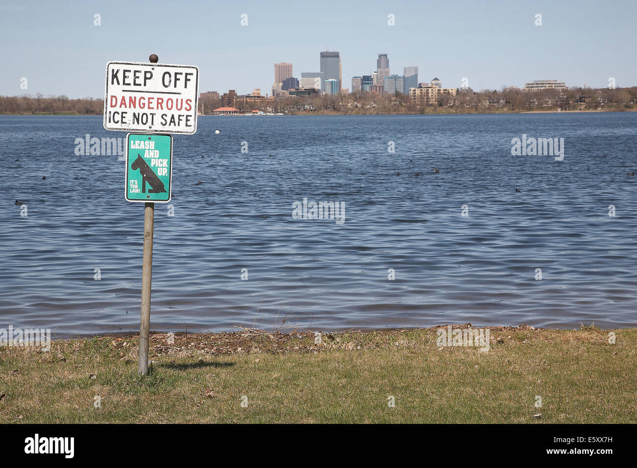 Ein Warnschild am Ufer des Lake Calhoun mit der Stadt von Minneapolis in der Ferne. Stockfoto