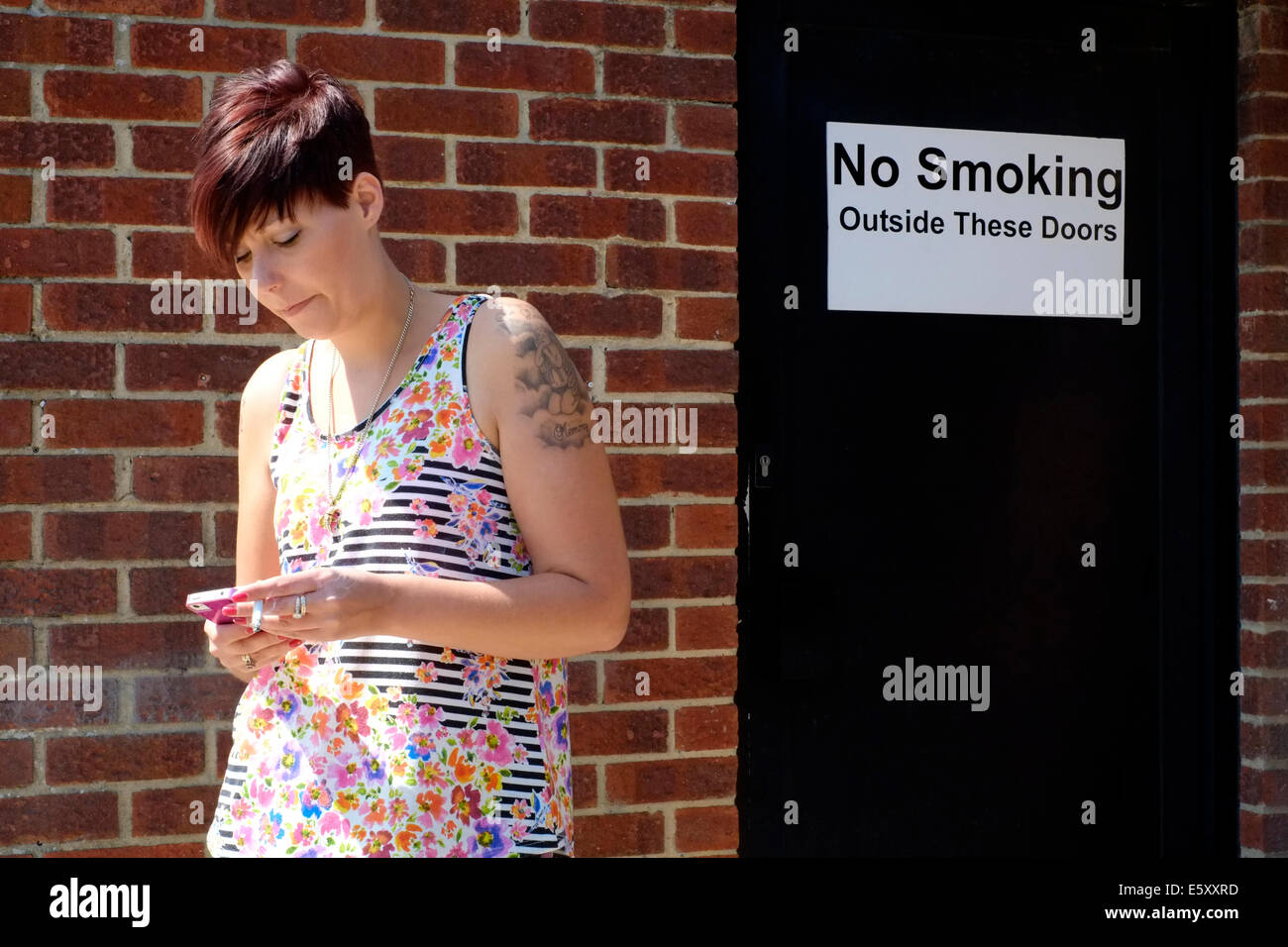 junge Frau mit Zigarette und Handy vor keine Rauchen Zeichen Stockfoto
