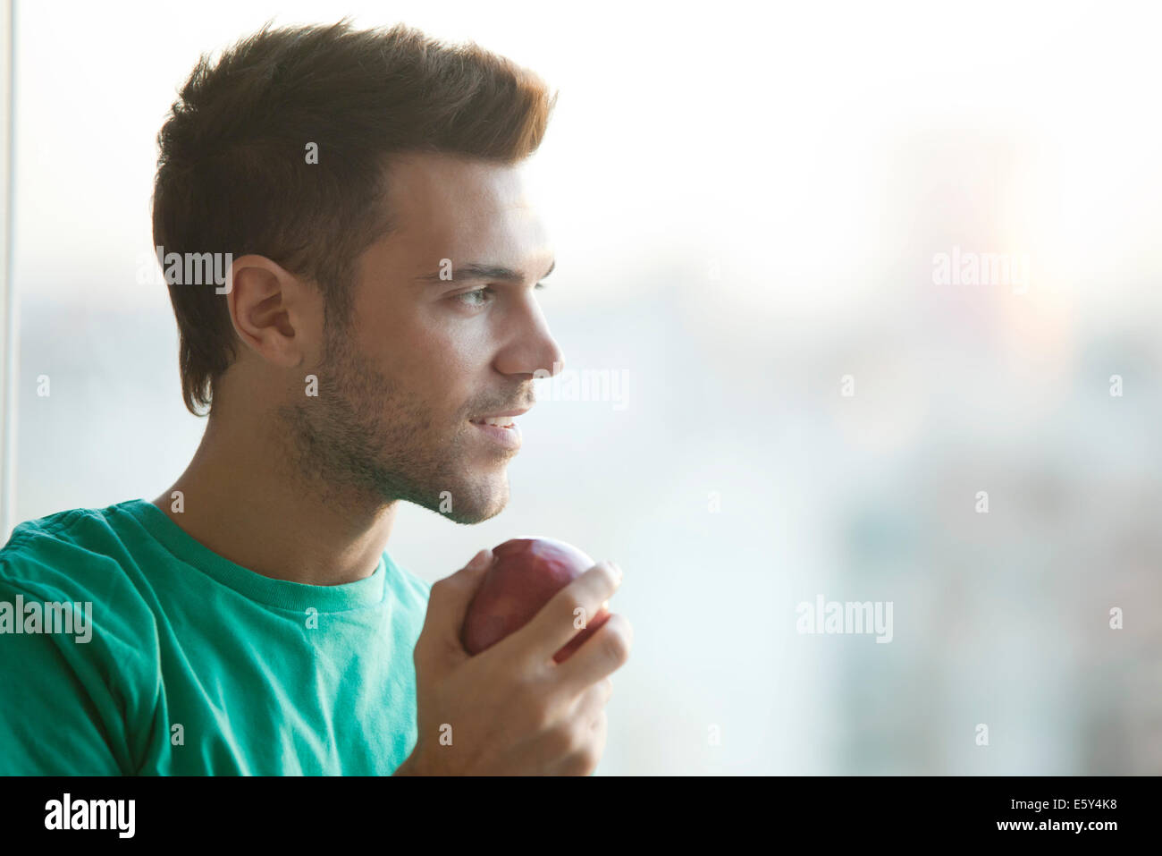 Mann hält Apfel, Blick aus Fenster Stockfoto