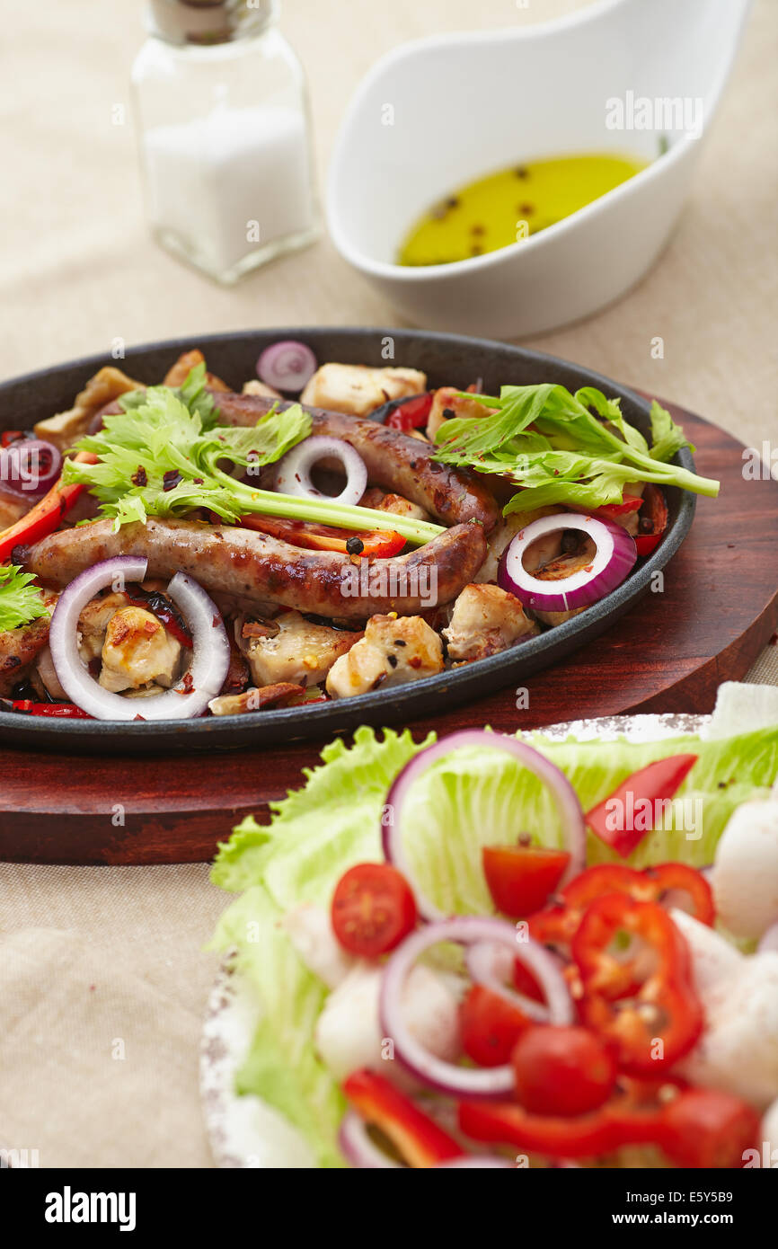 gebackene gewürfelten Huhn und Wurst mit Zwiebeln, Paprika, Mushrrooms und einem Salat aus Tomaten, Champignons, Paprika und Salat. Stockfoto