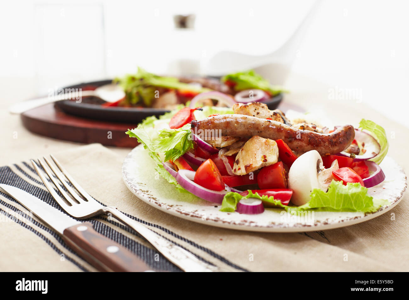 gebackene gewürfelten Huhn und Wurst mit Zwiebeln, Paprika, Mushrrooms und einem Salat aus Tomaten, Champignons, Paprika und Salat. Stockfoto