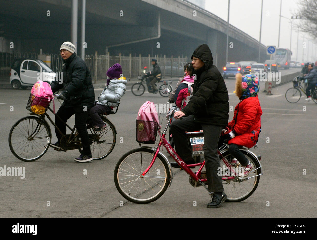 Zwei Männer auf Fahrrädern, ihre Kinder zur Schule schicken morgens in Peking mit Smog eingehüllt. Stockfoto