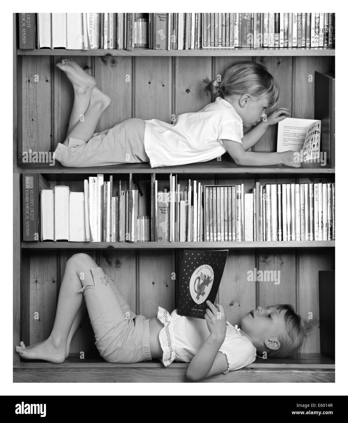 Junge Mädchen, die Bücher zu lesen, während im Bücherregal liegend Stockfoto