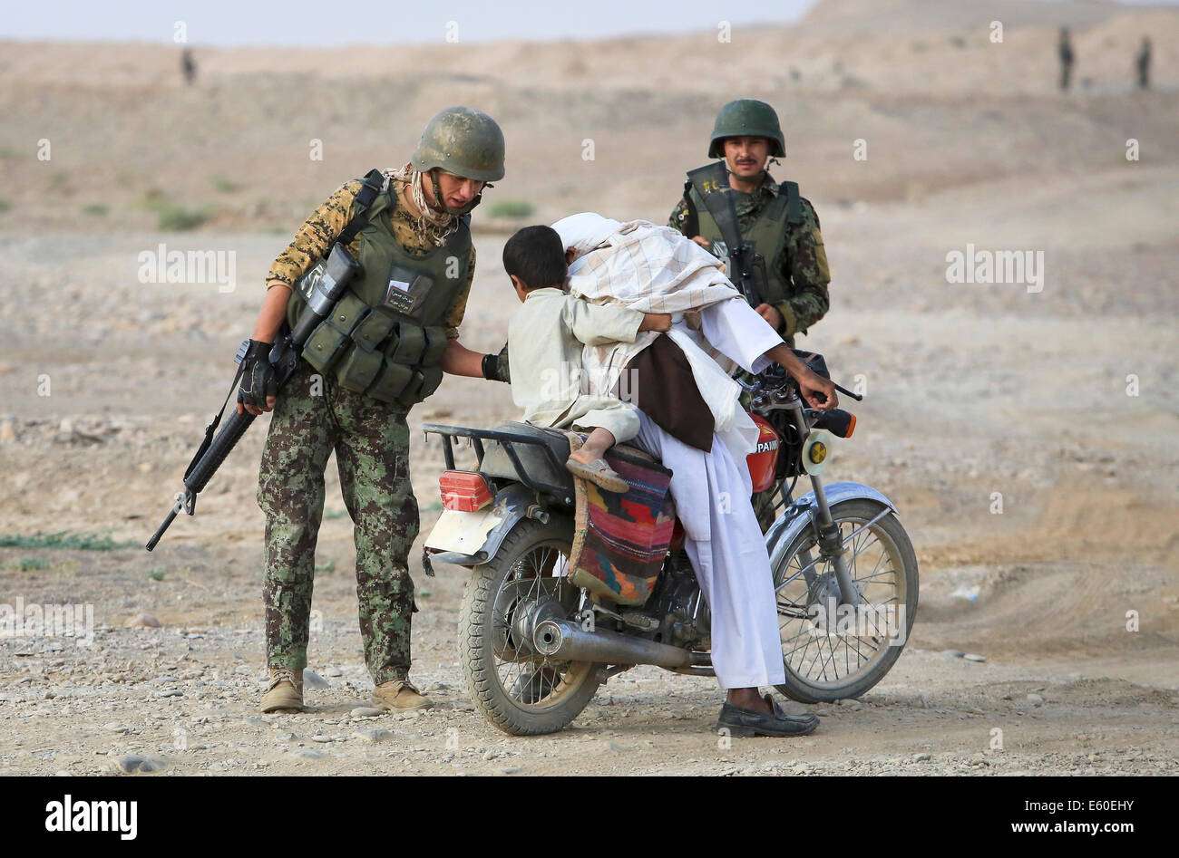 Afghanische Zivilisten auf einem Motorrad sind durch ein Afghan National Army Soldat an einem Checkpoint Fahrzeug gestoppt 14. Juli 2014 im Dorf Shekasteh Tappeh, Provinz Helmand, Afghanistan, 14. Juli 2014. Stockfoto