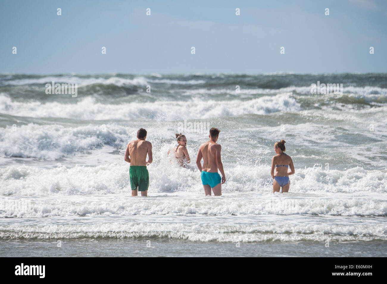 Borth, Ceredigion, Wales, UK. 10. August 2014.High Winde an der Küste als das Endstückende des Hurrikan Bertha geht.  In einer Pause in das Wetter, eine Gruppe von Jugendlichen genießen genießen Sie einem kurzen Zwischenspiel Sonnenschein spielen im Meer am Borth, in der Nähe von Aberystwyth Ceredigion Wales UK Credit: Keith Morris/Alamy Live-Nachrichten Stockfoto