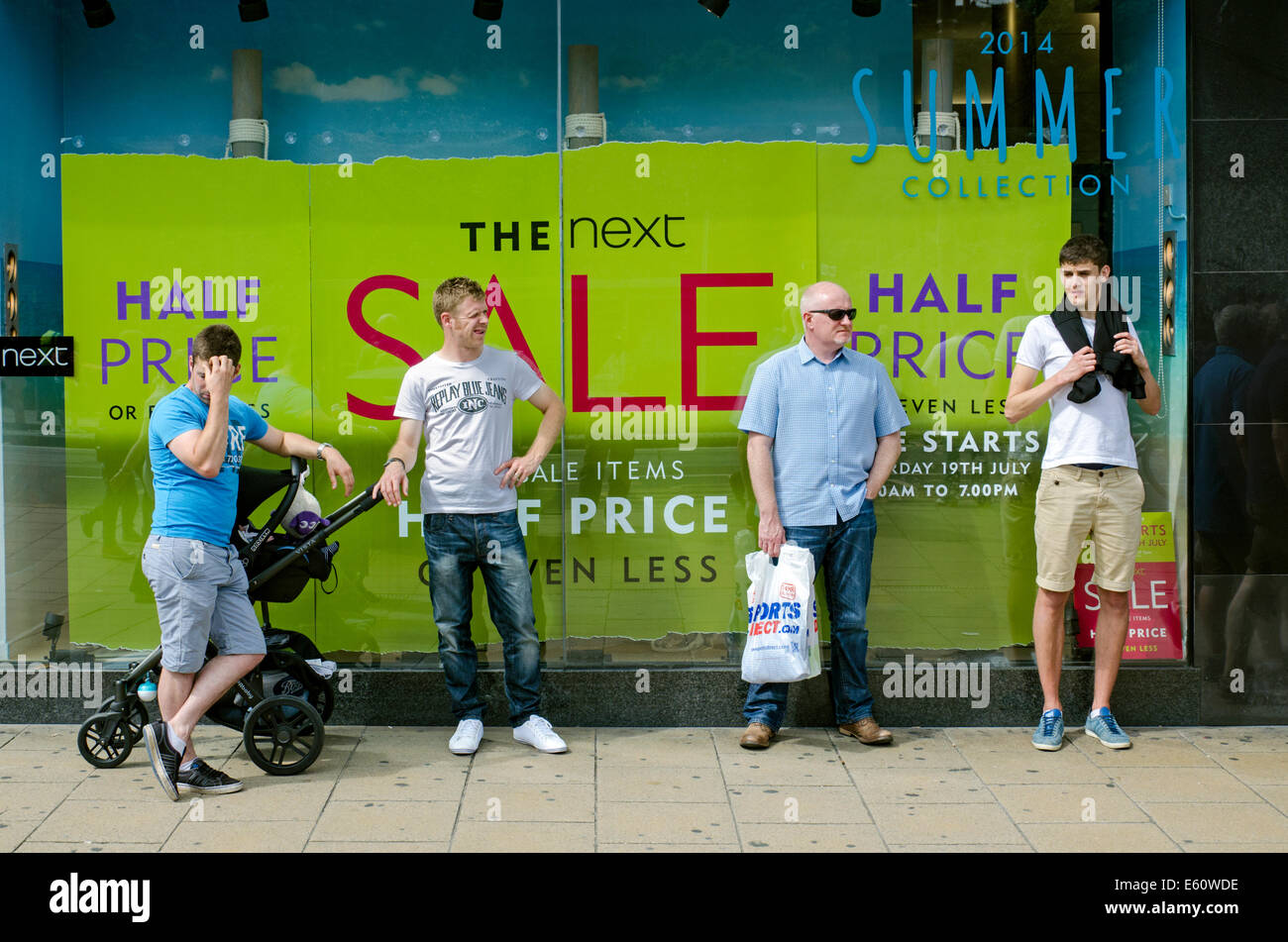 Vier Männer warten außerhalb der nächsten Verkauf auf Princes Street, Edinburgh, während ihre Partner im Inneren sind. Stockfoto