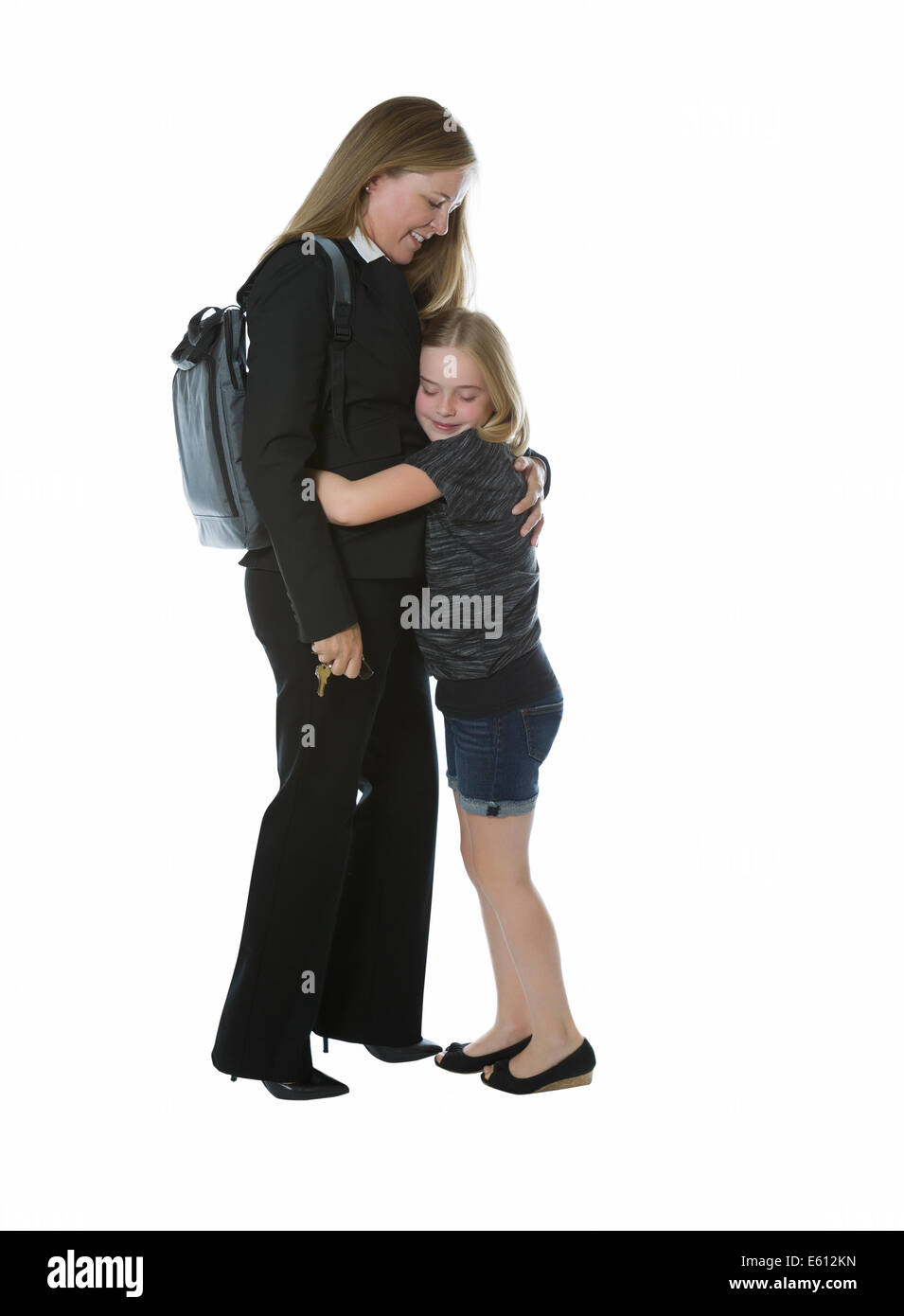 Seitenansicht der Geschäftsfrau und ihrer kleinen Tochter umarmt sie, wenn Sie nach Hause von der Arbeit während isoliert auf weißem Hintergrund Stockfoto