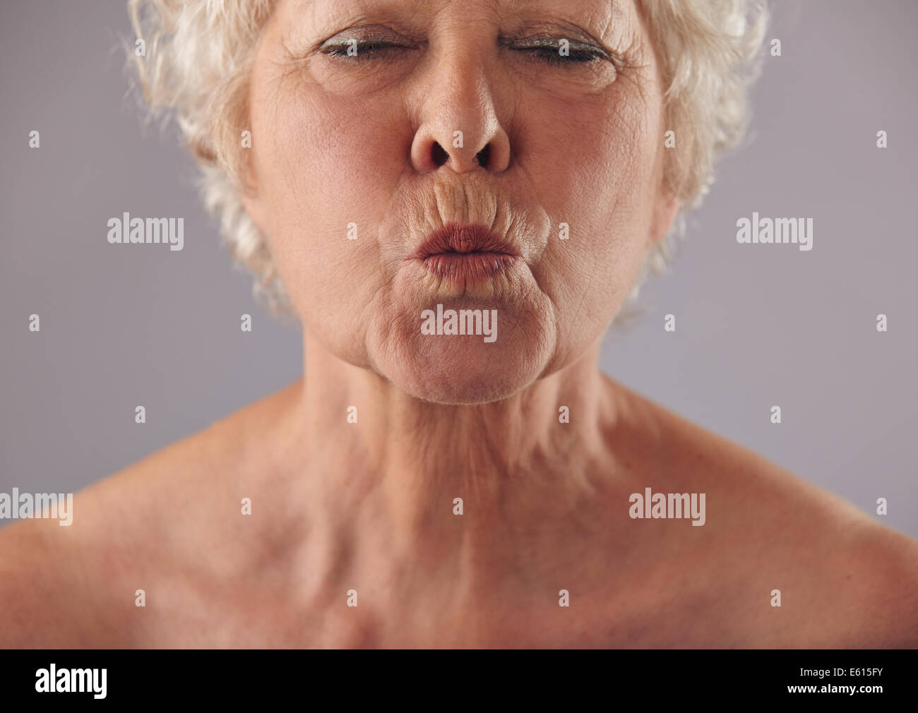Porträt von senior Frau Lippen Kräuseln beschnitten. Reife Frauen Grimassieren vor grauem Hintergrund Stockfoto