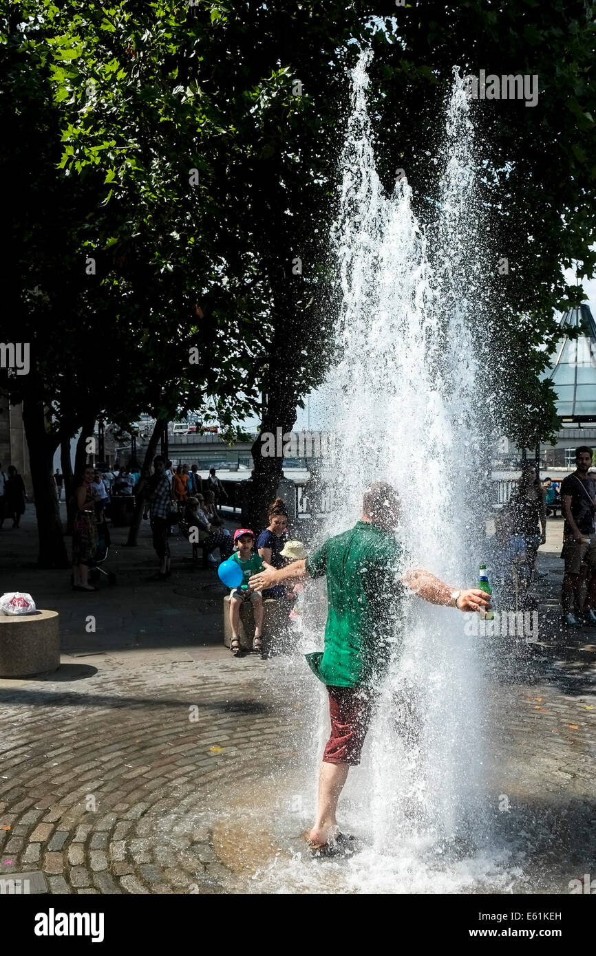 Ein Mann mit einer Flasche Bier läuft in eine Quelle des Wassers, das heiße Wetter in London zu entkommen. Stockfoto