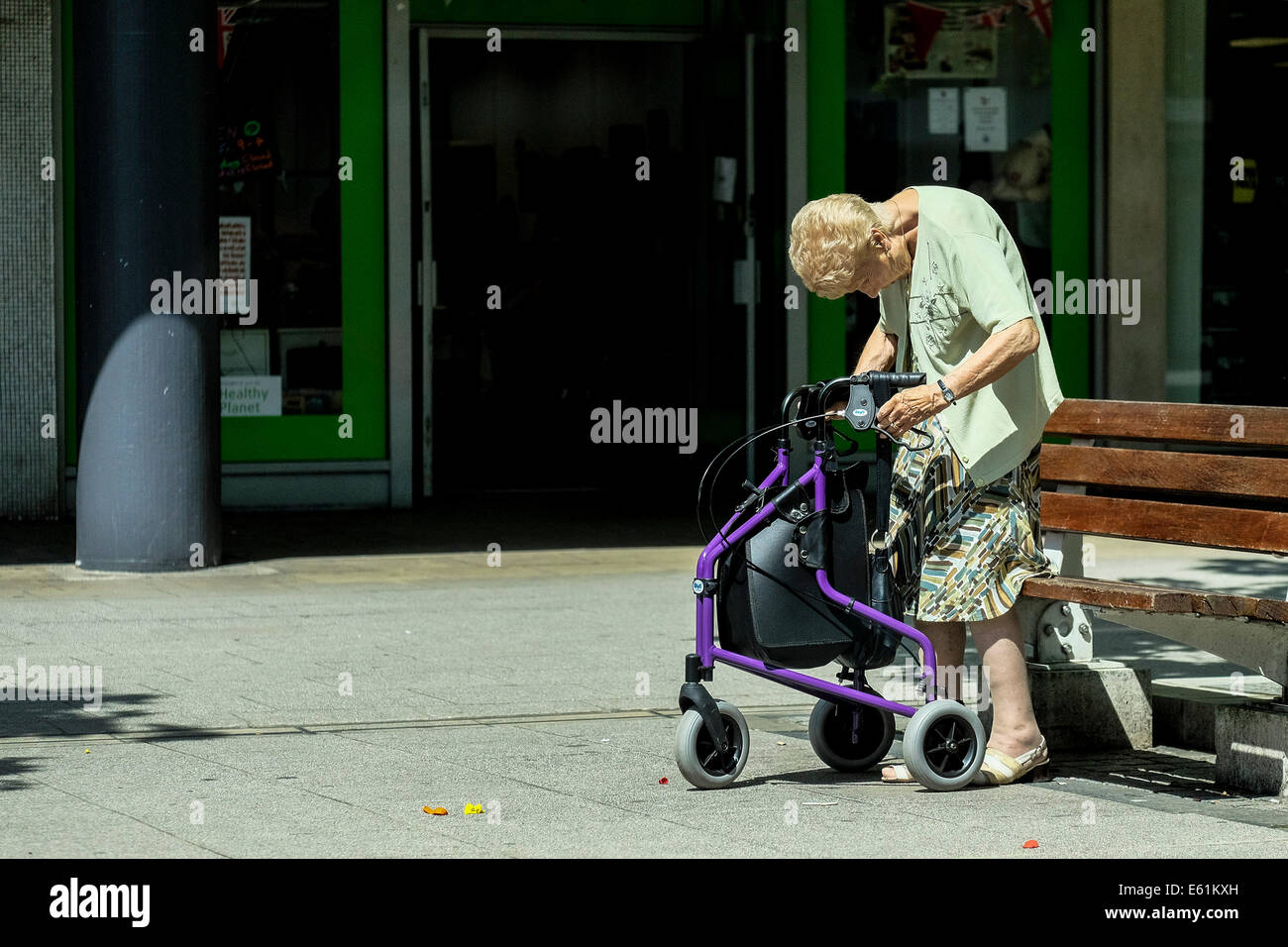 Eine alte Dame mit eingeschränkter Mobilität zu sitzen auf einer Bank. Stockfoto