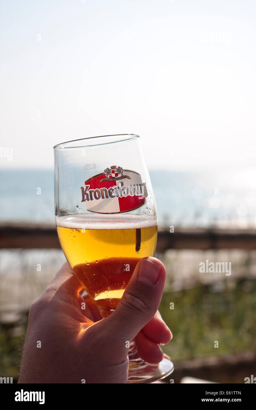 Eine Hand hält ein Glas Bier hell und sonnig Meer im Hintergrund Stockfoto