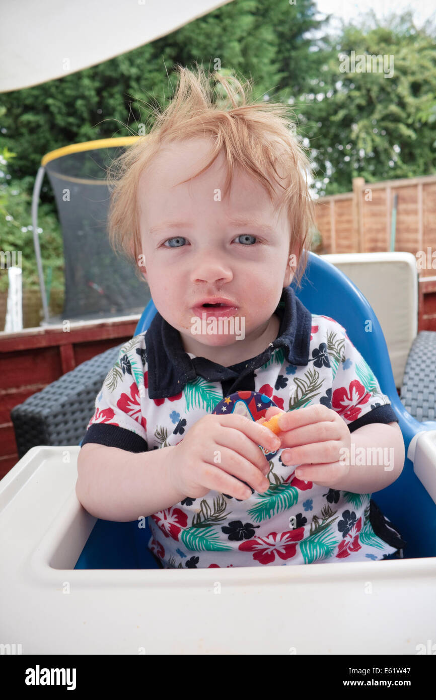 Ein einjähriger Junge sitzt in einem Hochstuhl Essen Chips Stockfoto