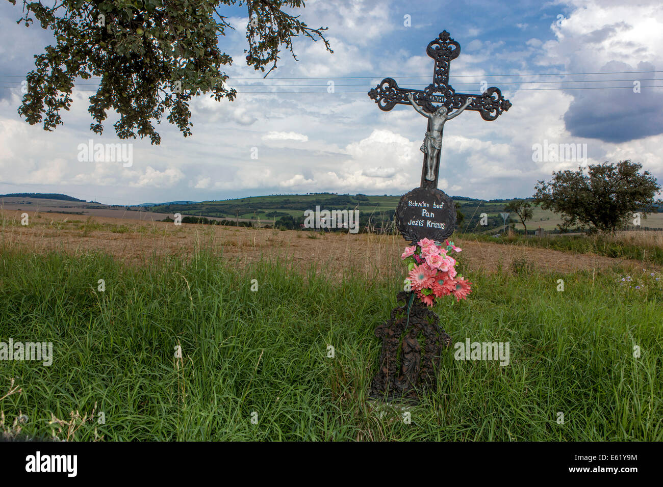 Christian Kreuz mit Jesus und rotem Kunststoff Blumen im Land Stockfoto