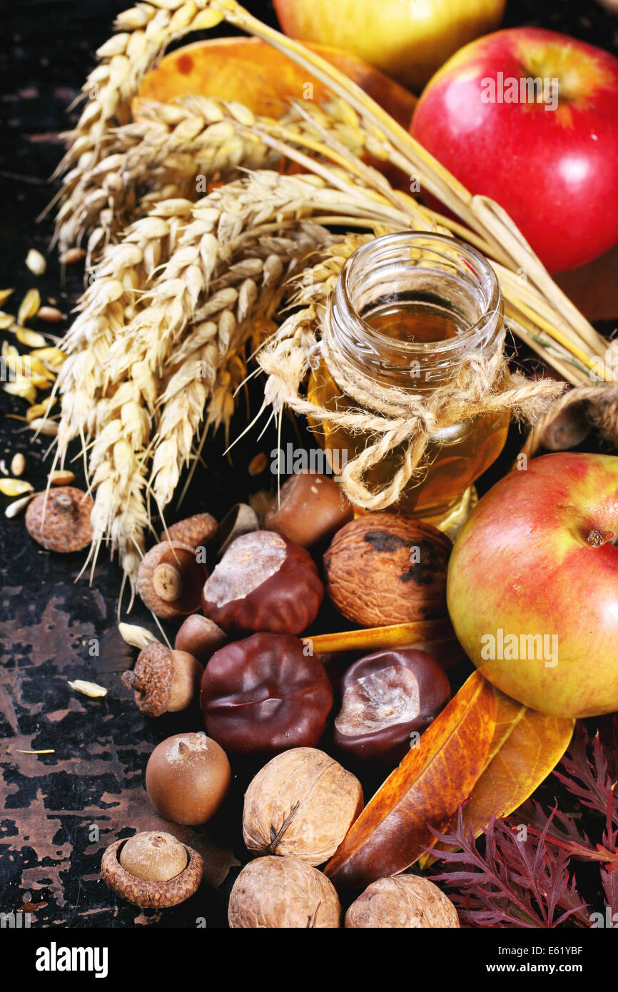 Glasglas Honig mit Äpfel, Ohren von Weizen, Kastanien und Walnüsse über schwarzer Holztisch Stockfoto