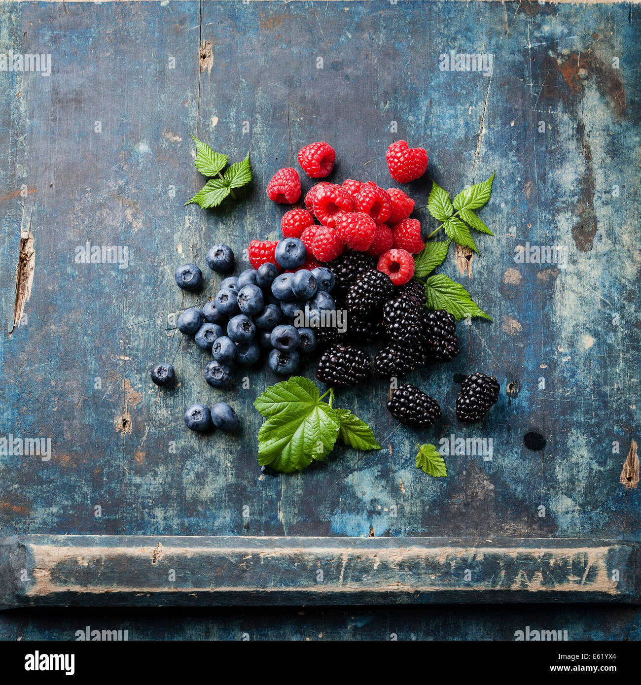 Mischung aus frischen Beeren mit Blättern auf blauem Hintergrund aus Holz Stockfoto