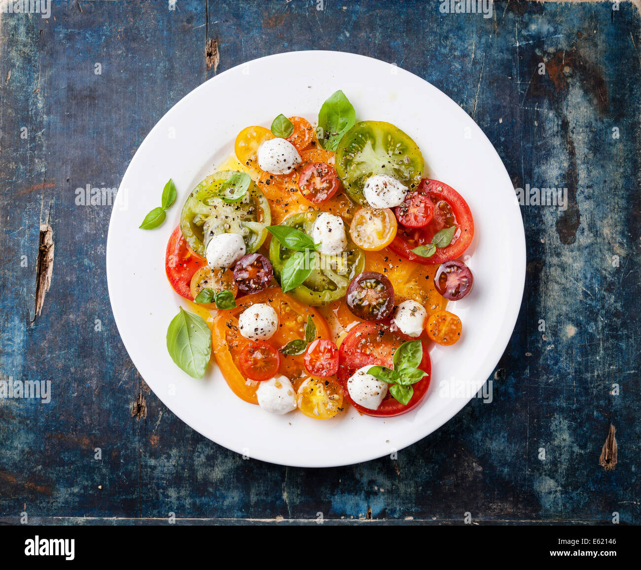 Bunte Tomaten-Salat mit Mozarella auf blauem Hintergrund aus Holz Stockfoto