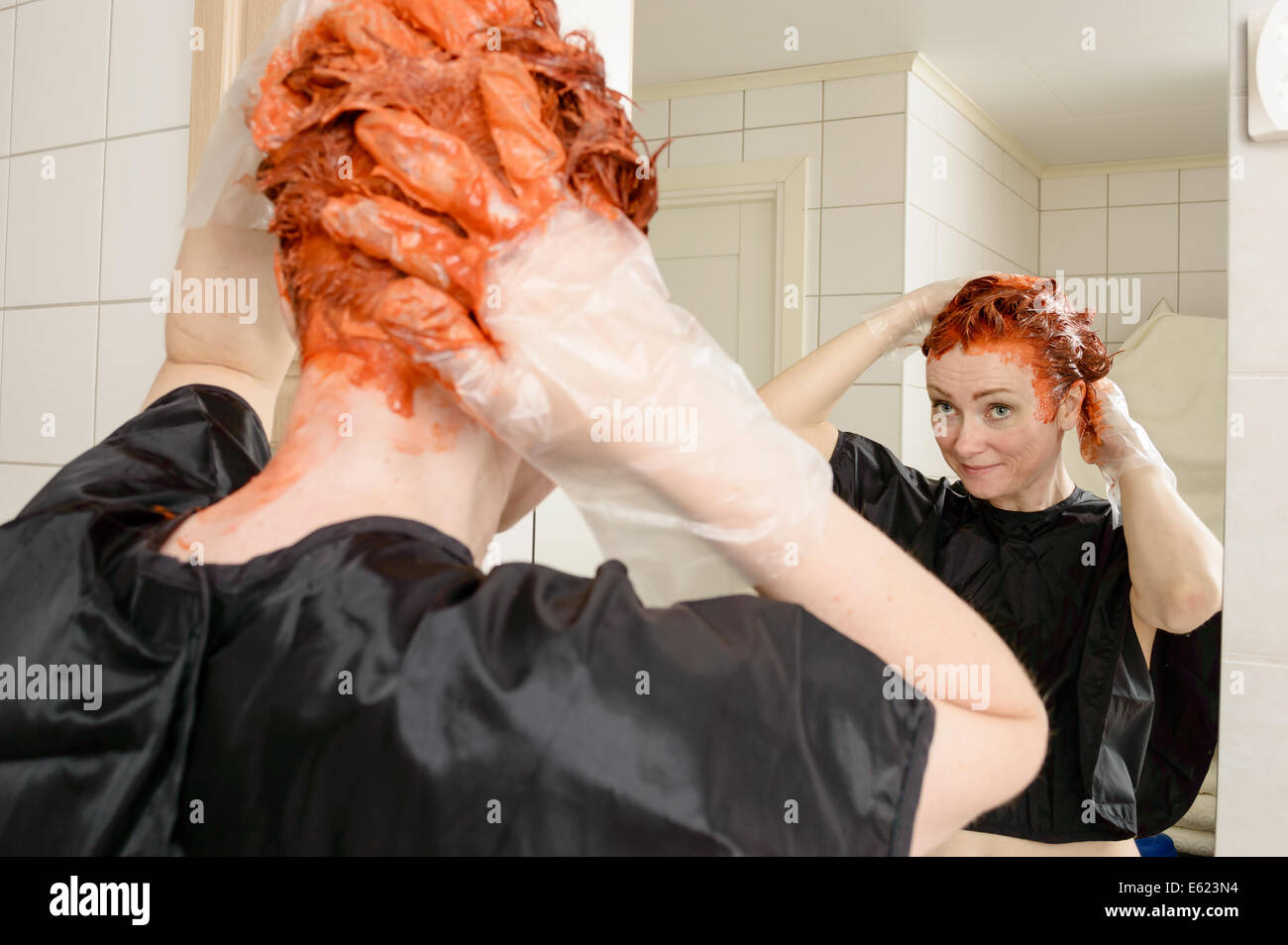 Kaukasische Frau mit kurzen Haaren sterben ihr Haar rot vor Spiegel in ihrem eigenen Badezimmer. Stockfoto