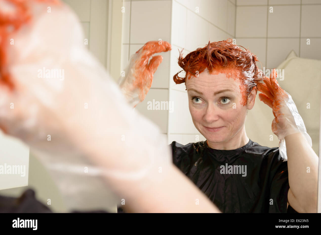 Kaukasische Frau mit kurzen Haaren sterben ihr Haar rot vor Spiegel in ihrem eigenen Badezimmer. Stockfoto