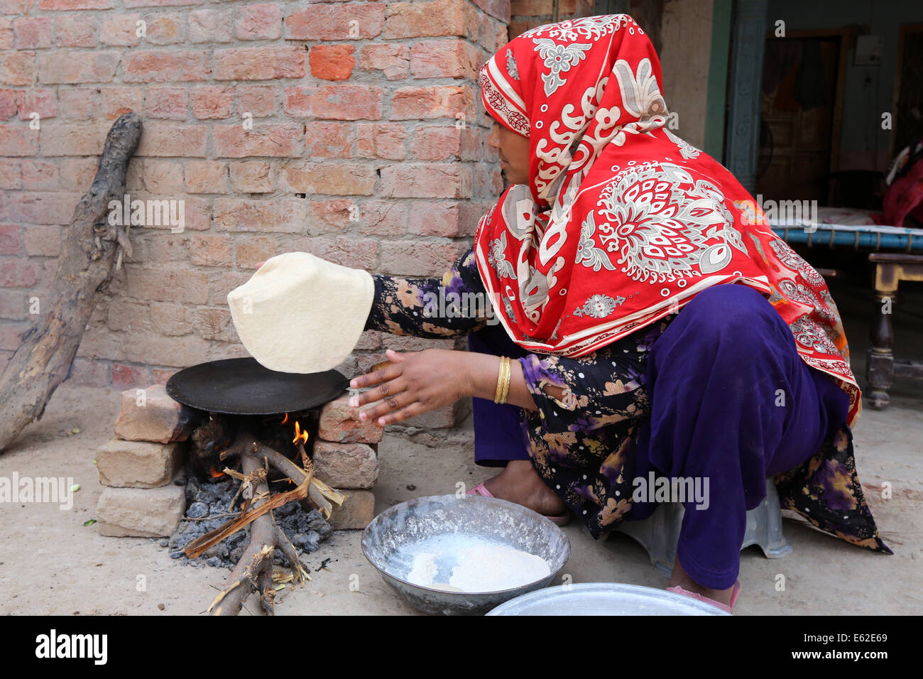 Frau in traditioneller Kleidung Roti Brot (auch bekannt als Chapati) am offenen Feuer backen. Khushpur Dorf, Provinz Punjab, Pakistan Stockfoto