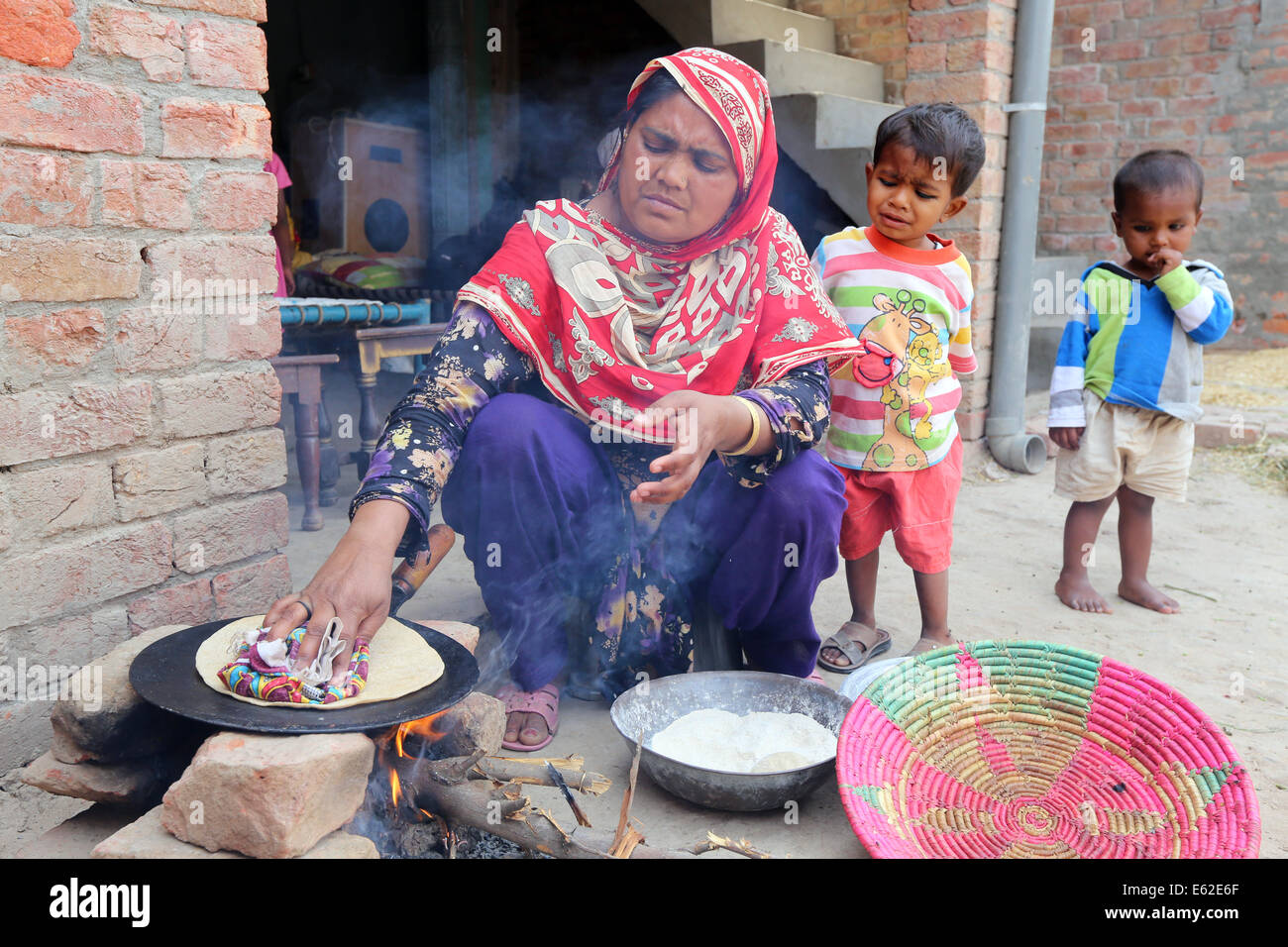 Frau in traditioneller Kleidung Roti Brot (auch bekannt als Chapati) am offenen Feuer backen. Khushpur Dorf, Provinz Punjab, Pakistan Stockfoto