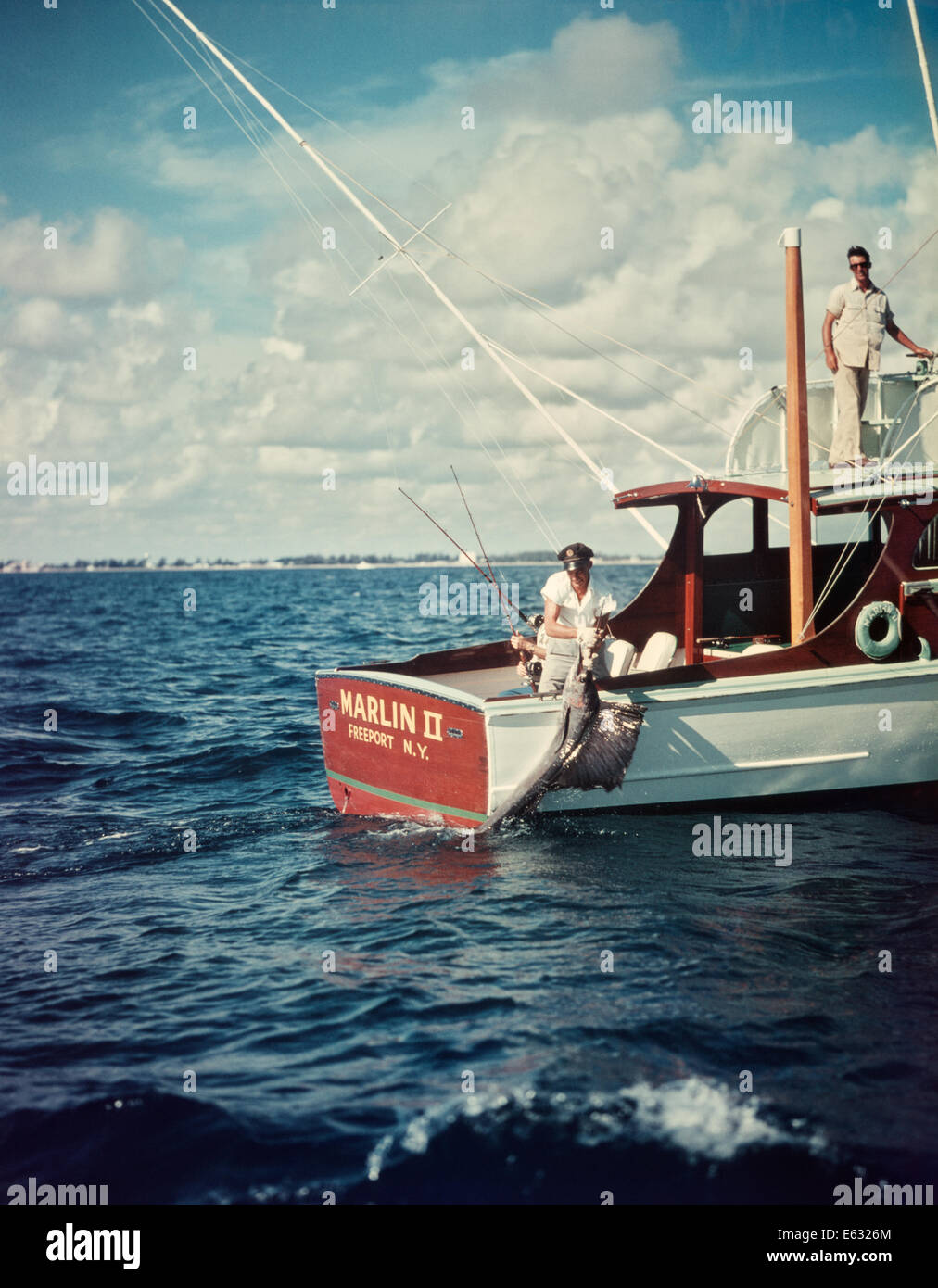 1950ER JAHRE DEEP SEA FISHING BOOT MANN ZIEHEN AN BORD GEFANGENEN FÄCHERFISCH Stockfoto