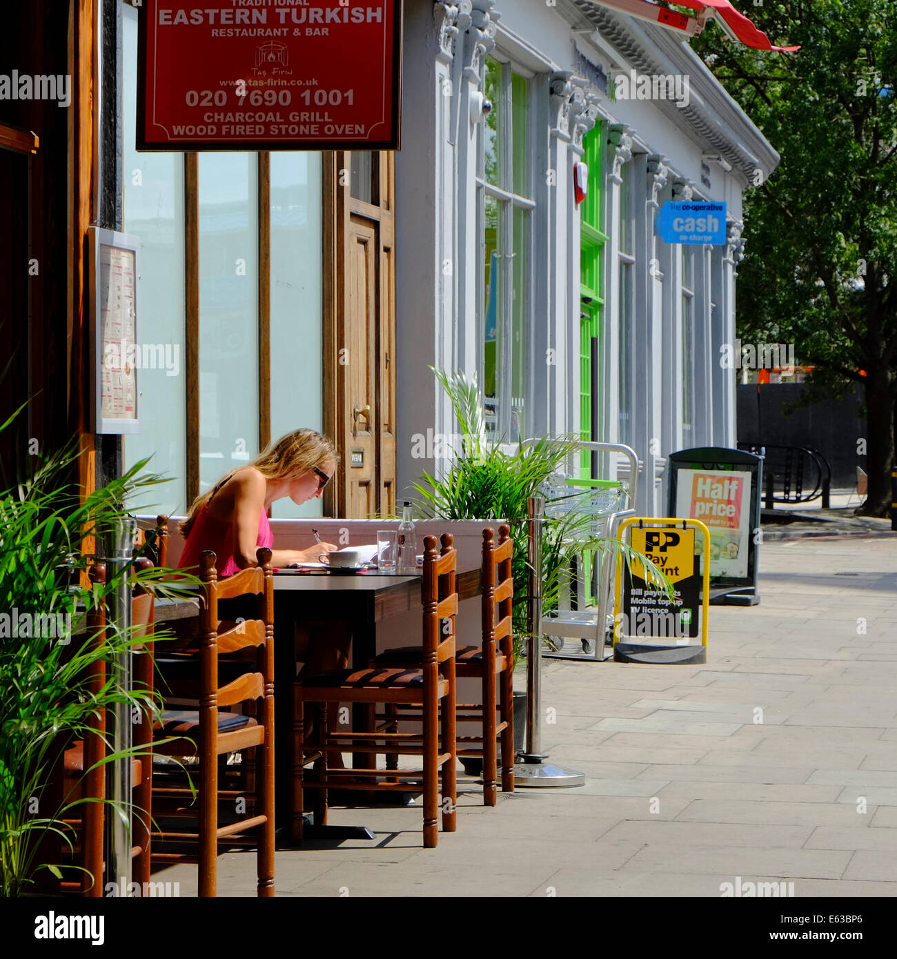 blonde Frau sitzt schreiben Brief & Kaffeetrinken in Ost-türkischen Restaurant in London Stockfoto
